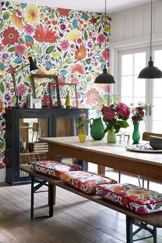 a dining room table with flowers on the wall behind it and two vases filled with flowers