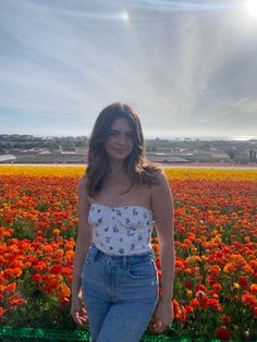 a woman standing in front of a field full of orange and red flowers with the sun behind her