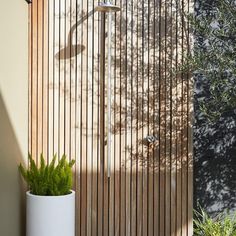 a tall white planter sitting next to a wooden wall with vertical slats on it