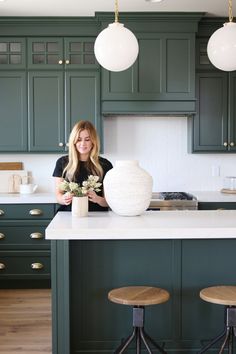 a woman standing in a kitchen with green cabinets