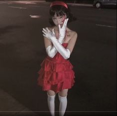 a woman dressed in red and white holding her hands up to her face while standing on the street