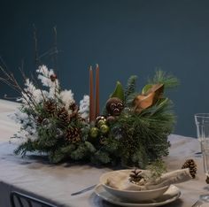 the table is set for christmas dinner with pine cones and greenery