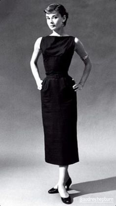 a woman in a black dress standing with her hands on her hips and looking at the camera