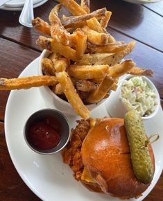 a white plate topped with a sandwich and fries next to coleslaw on a table