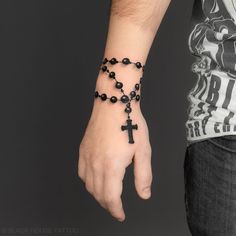 a person wearing a black rosary bracelet with a cross on it's wrist,