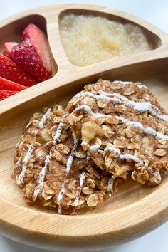 a wooden plate topped with cookies covered in icing next to strawberries and oatmeal