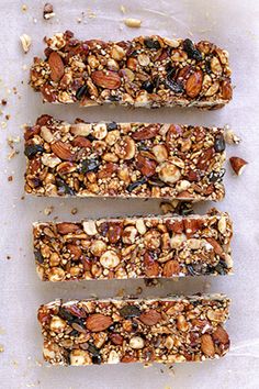 three granola bars are lined up on a sheet of parchment paper with nuts and seeds