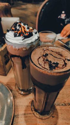 two drinks sitting on top of a wooden table covered in chocolate and whipped cream toppings