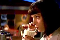 a woman drinking from a coffee cup while talking on her cell phone and holding a straw in her mouth