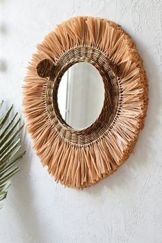 a round mirror hanging on the wall next to a palm leaf potted in front of it