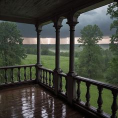 a porch with wooden railings and columns under a cloudy sky over a green field