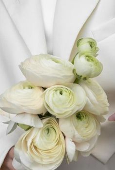 a woman holding a bouquet of white flowers in her hands and wearing a white jacket