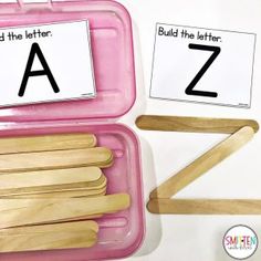 two pink trays with wooden utensils in them and the letters a to z