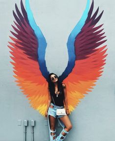 a woman standing in front of a wall with large colorful wings on her head and arms