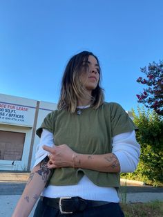 a woman standing in front of a building with her arms crossed and tattoos on her arm