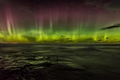 an aurora bore is seen in the sky above water and clouds, with green and purple lights