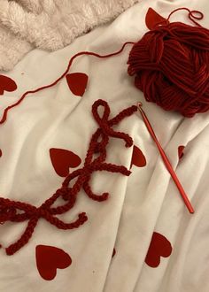 a ball of yarn and knitting needles laying on a bed with hearts drawn on it