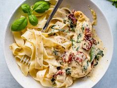 a white bowl filled with pasta and spinach on top of a blue tablecloth