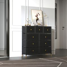 a black dresser with gold knobs in a white room next to a painting on the wall