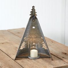 a candle is lit in front of a metal triangle shaped christmas tree on a wooden table