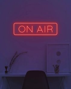 a neon sign that reads on air above a desk with a chair and plant in the corner