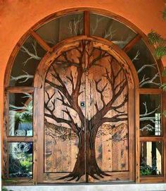 an open wooden door with a tree painted on the front and side glass panels above it