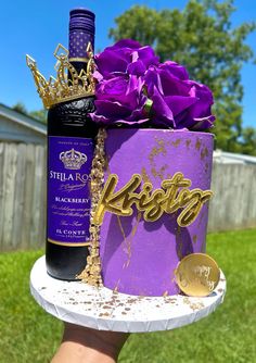 a purple cake with a bottle of wine on it and some gold decorations in the middle