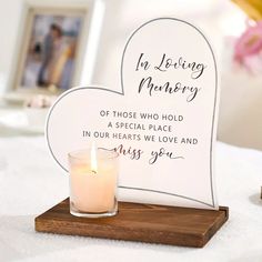 a white heart shaped sign with a candle on it next to a vase and flowers