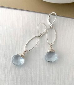 These beautiful faceted aquamarine quartz drop dangle earrings are available in vermeil gold or sterling silver.  They aquamarine heart briolettes are simply wire wrapped and dangle from textured, laser cut medium oval hoops finished with gold filled or sterling silver lever backs. Dainty & elegant dressed up or down.  These earrings make a perfect gift for a March birthday girl, bridesmaid or a special girl on any occasion! The earrings measure just approx 2" from end to end.  The aquamarine quartz approx 12mm.  Please make your preferred metal selection from the drop down menu at check out. If you should need multiple pairs please do not hesitate to contact me.  You may also like to check out more of my aquamarine jewelry here:  http://etsy.me/2FQujDr You may like to check out more of my Wire Wrapped Briolette Earrings, Blue Stone Earrings, Emma Style, Gemstone Hoop Earrings, March Birthday, Bling Earrings, Aquamarine Jewelry, Special Girl, Drop Dangle Earrings