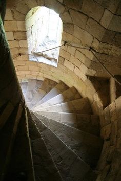 a spiral staircase in an old stone building with a light coming from the window above it