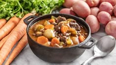 a pot filled with stew next to carrots and potatoes