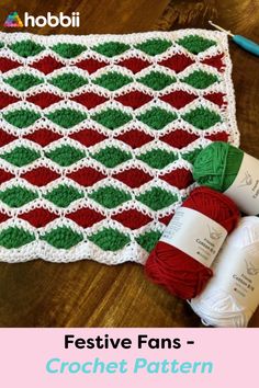 a crocheted afghan with red, green and white yarn next to two balls of yarn