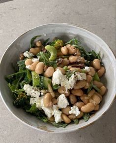 a white bowl filled with beans and broccoli on top of a marble table