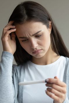 a woman holding a pen and looking at her cell phone while she holds her head