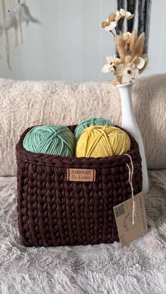 two balls of yarn sit in a basket next to a white vase filled with flowers