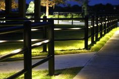 a row of benches sitting on top of a grass covered field at night with lights in the background