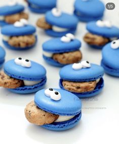 blue macaroons with googly eyes are on a white surface and one cookie is in the shape of a fish