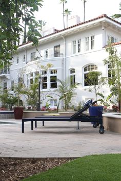 a bench in front of a large white building with palm trees and potted plants