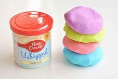 a can of whipped cream next to three colored doughnuts on a white surface