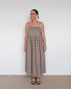 a woman standing in front of a white wall wearing a brown dress and black sandals