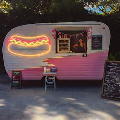 a pink and white trailer with a neon hot dog sign