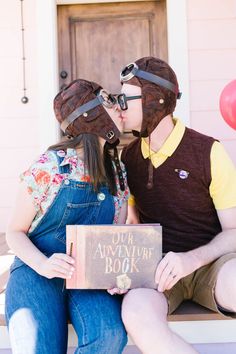 a man and woman sitting on a bench kissing while holding an adventure book in front of them