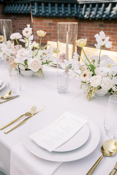 a table set with white and gold place settings, silverware and flowers in vases