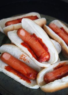 several hotdogs with ketchup on them are sitting in a black plate