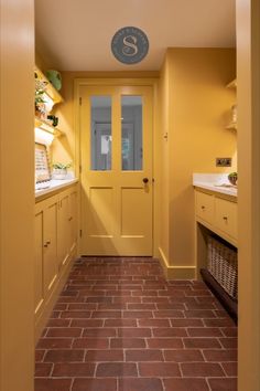 a yellow door is in the middle of a hallway with red brick flooring and cabinets