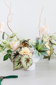 a white vase filled with flowers and greenery on top of a table next to scissors