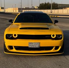 the front end of a yellow sports car parked in a parking lot with its lights on