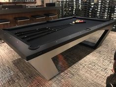 a pool table in the middle of a room with many bottles on the wall behind it