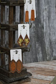 wooden earrings hanging from hooks on a stand with wood planks behind them and an earring holder in the foreground