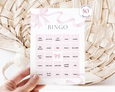 a person holding up a pink and white printable baby shower game with bows on it